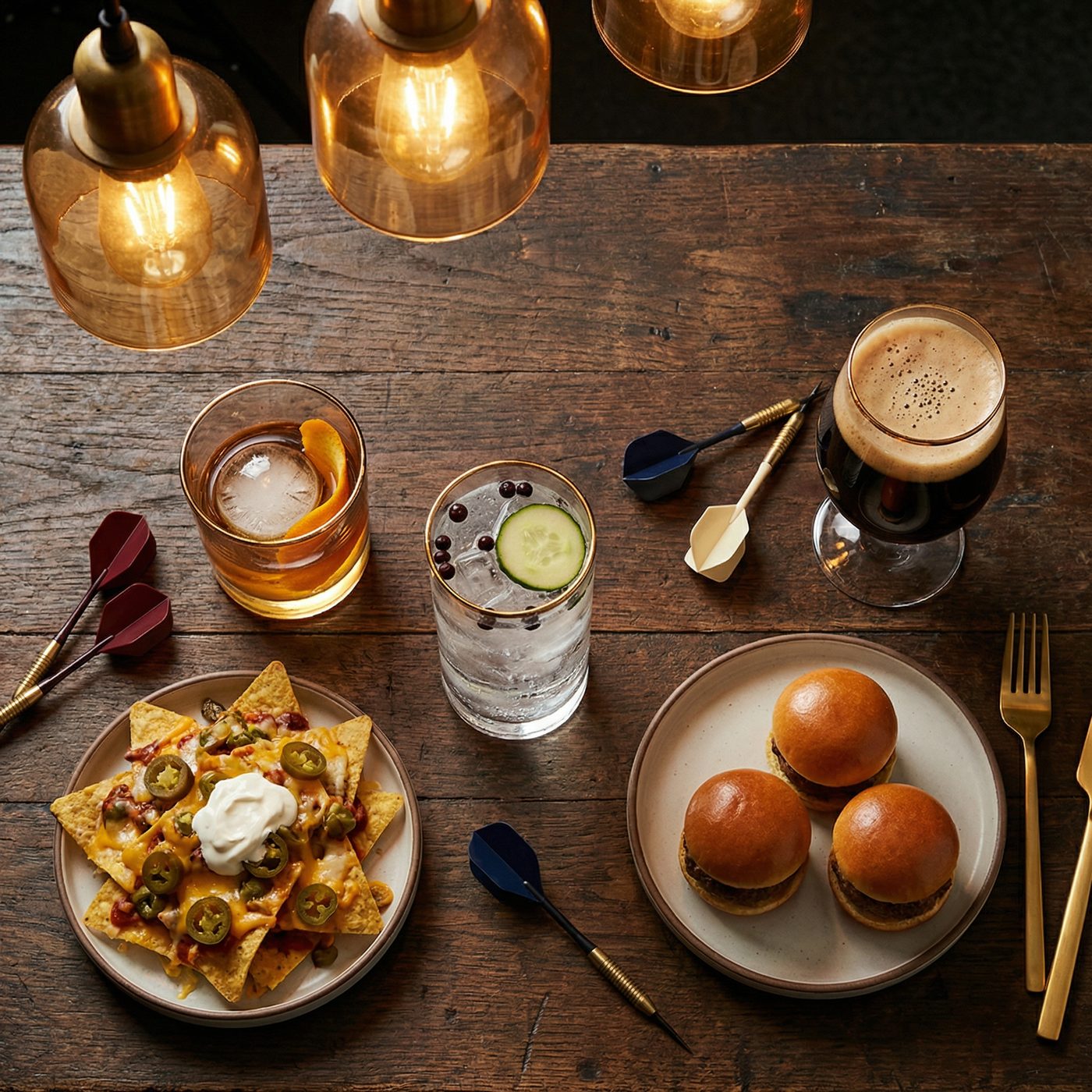 Cocktails, beer, nachos and sliders on a bar top with darts